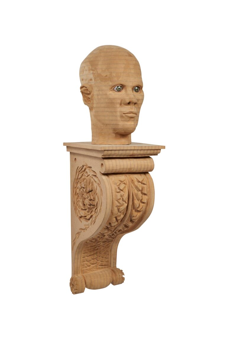 A wooden carving of a head on a shelf.