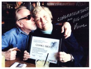 A person holding up a certificate and another person kissing the cheek of the other person.