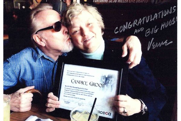 A person holding up a certificate and another person kissing the cheek of the other person.