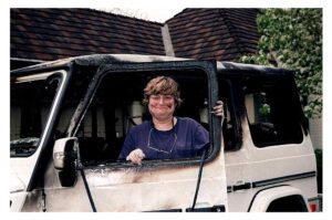 A person standing in a car door of a burnt car.